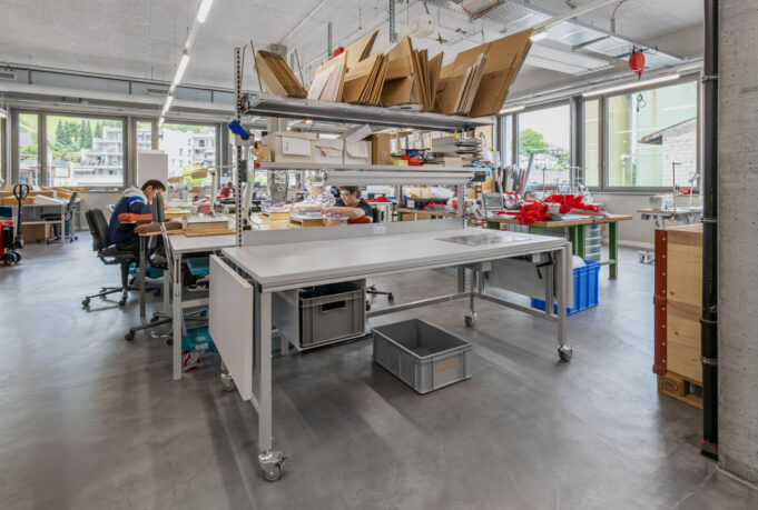 ERGO-Basic packing table with castors in a well-lit workshop with storage racks and staff